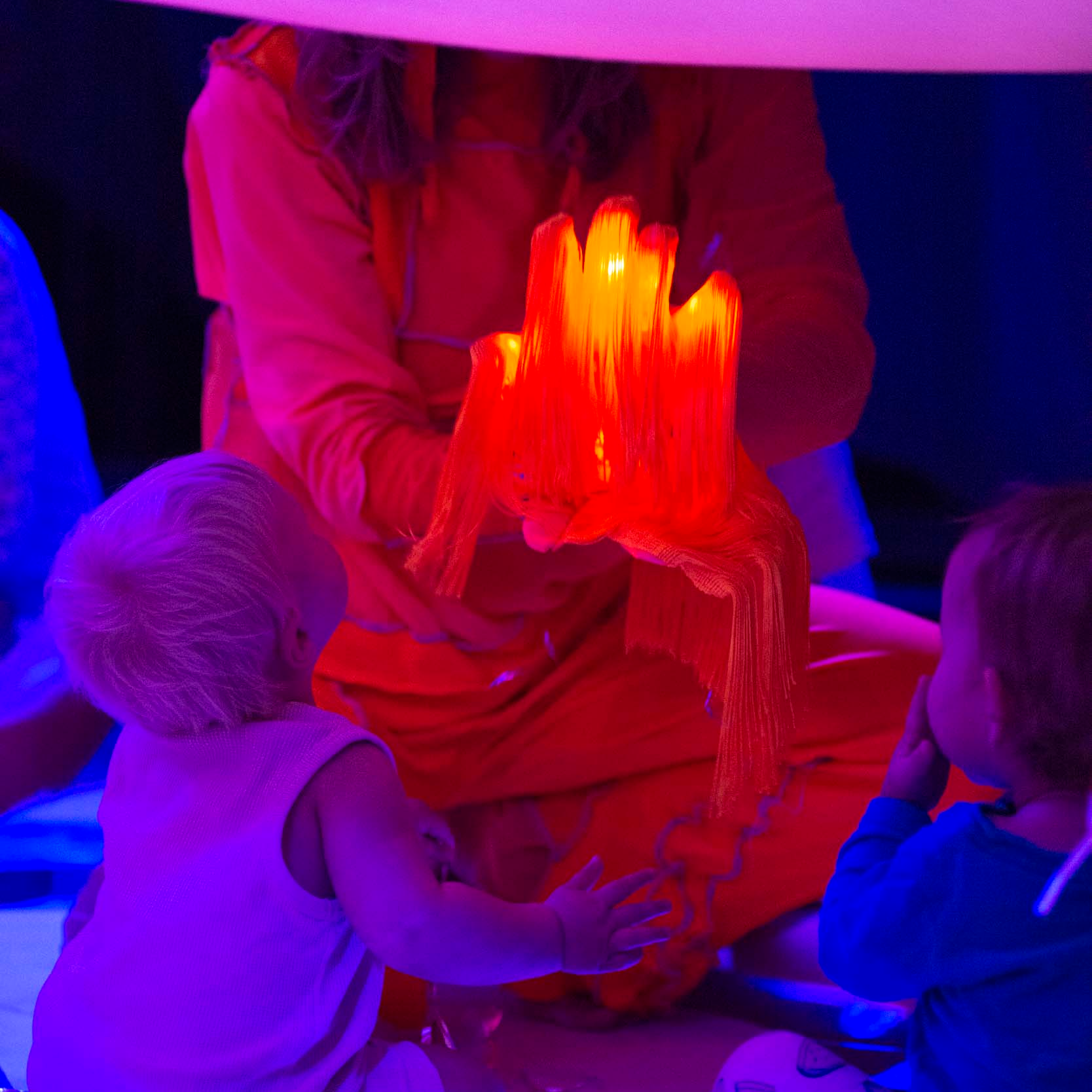 A baby is admiring a piece of fabric with lights inside in the performance Untz baby untz. 